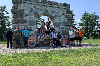 Landmark College hiking class students posing in front of a large stone sculpture in Putney, Vermont.
