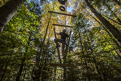 A student climbing the ropes course in the woods at Landmark College 