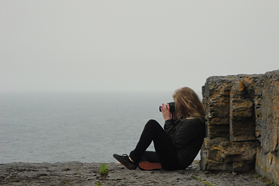 Student taking picture while sitting at the edge of the Cliffs of Moher