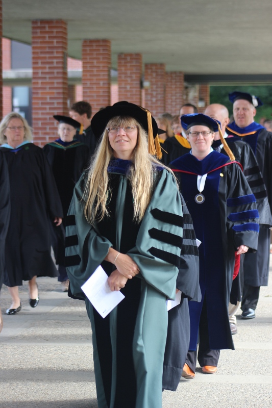 Faculty member in black cap and robe leads row of robed faculty through Landmark College colonnade