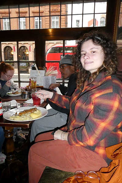 Female student poses for photo sitting at a restaurant table. She is holding her fork over a plate containing eggs, potatoes and sausage