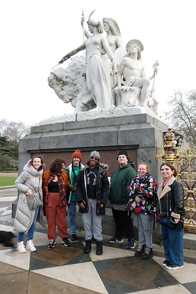 Seven students posing in front of large white sculpture of several heroic figures