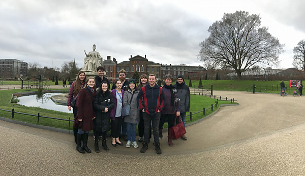 A group shot in Kensington Park. They are standing just in front of a monument surrounded by a small moat. In the far background is Kensington Castle.