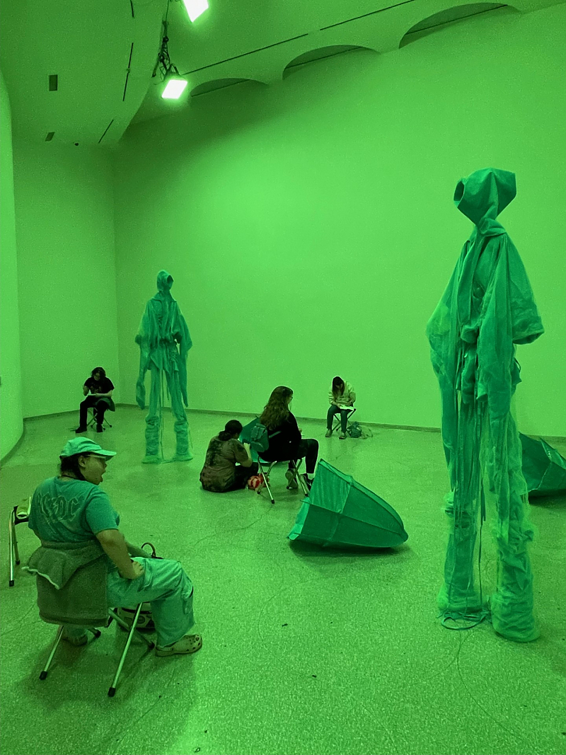 Students seated in various areas sketching sculptures inside a room illuminated with green light inside the Guggenheim museum