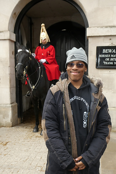 Student poses in front of an entryway in Buckingham Palace, from where a man on horseback is emerging