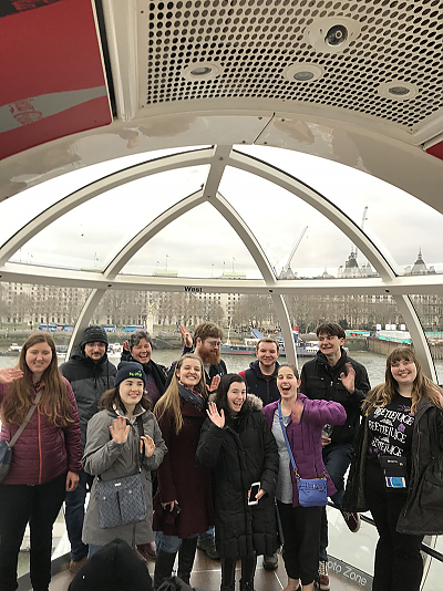 A groups shot of the students in the London Eye waving at the camera. Behind them is a view of a river and buildings.