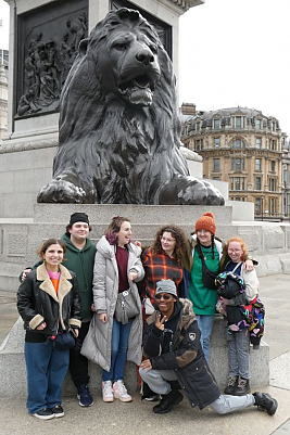 Seven students posing for a picture in front of large lion sculpture