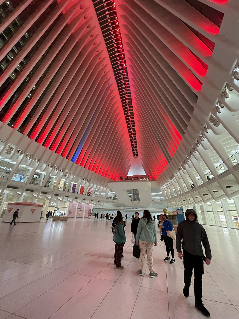 Students inside the Oculus, a large white structure with roof illuminated in red light