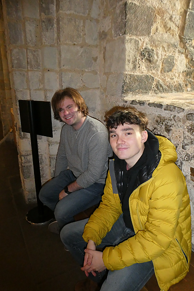 Two students smile at camera while seated in front an open air window