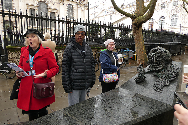 Students looking at a large sculpture made of dark stone on the streets of London