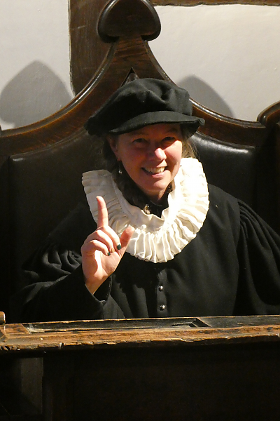 Dr. Adrienne Major wearing an Elizabethan school master's outfit while sitting in a large wooden chair