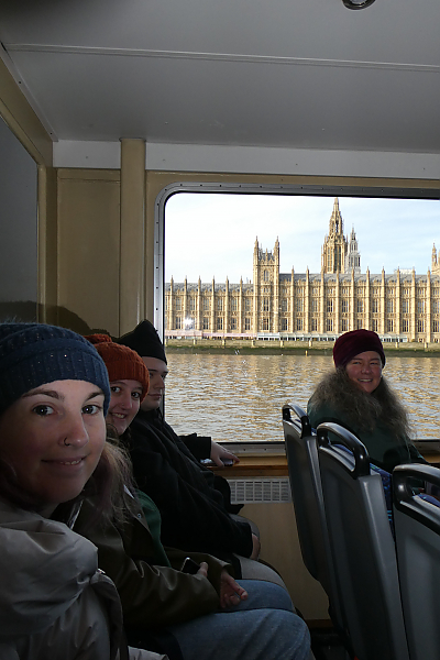 Members of London Study abroad group smile for camera while sitting inside a boat on the River Thames. A large building can be seen out the window.