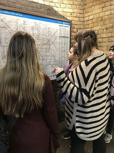 Looking over the shoulder of three female students as they read a map of London Rail and Tube system.