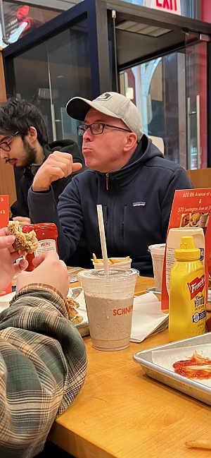 Picture across table of man in baseball cap eating French fries