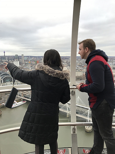 Two students atop the London Eye looking at the city's landscape. The female student on the left points at something out of view of the camera with a male student on the right looking in that direction.