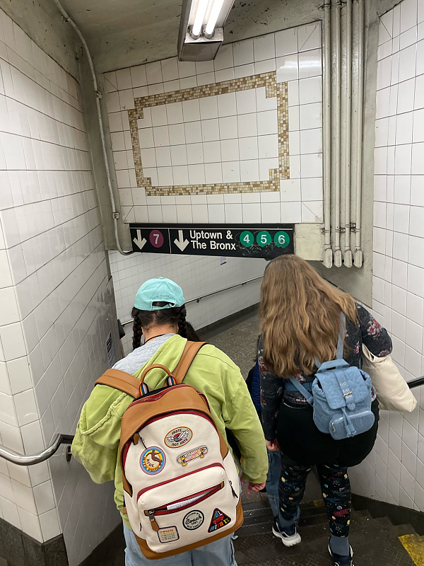 Watching two students wearing backpacks walk down the stairs into a subway station.
