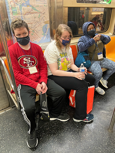 Three students sitting next to each other in a subway car. They are all wearing protective masks.