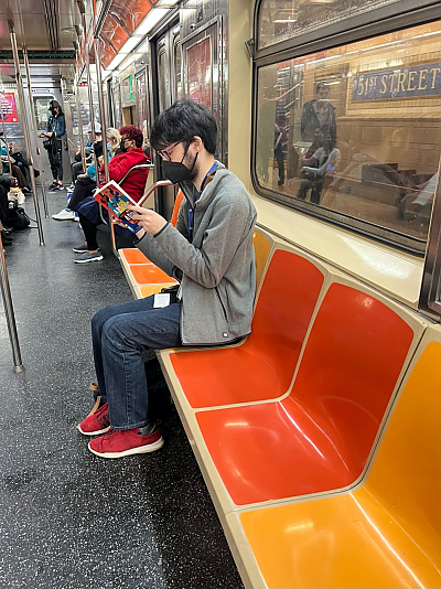 A male student sitting in subway car reading a book.