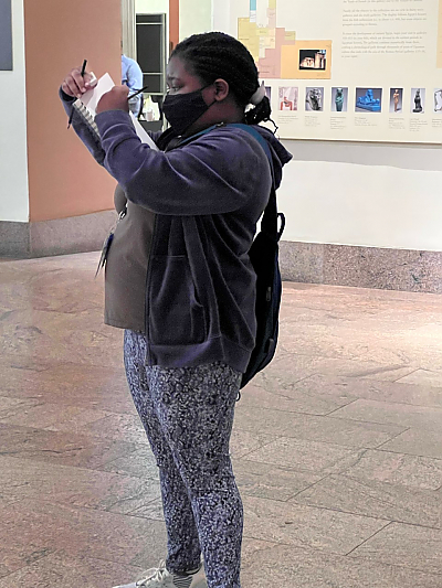 Student standing inside museum looking left of camera and sketching on a pad