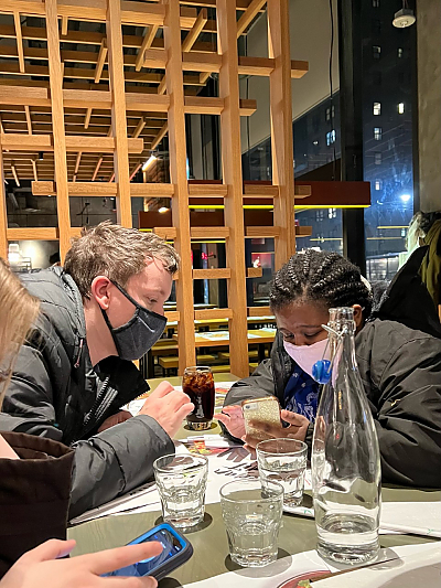 Students sitting across from each other at dinner table looking at a smartphone screen