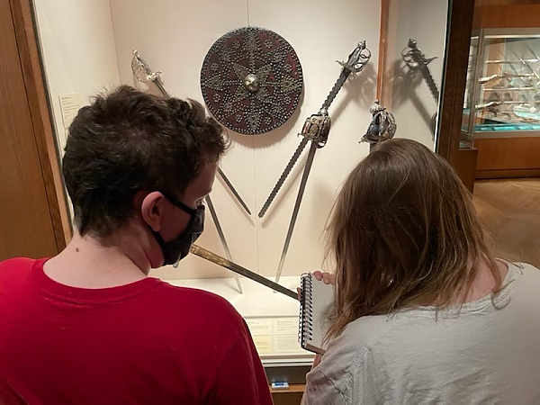 An over the shoulder picture of two students looking at an art exhibit of small disc and kniives.