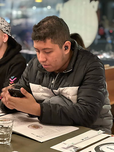 Male student sitting at table in restaurant looking at his phone screen
