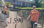 2 students stand on each side of a wrought iron gate that has the number 1590 on it. 