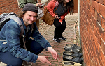 Three students in an outdoor alleyway. One of them is crouching down and pointing at a row of wooden shoes. 