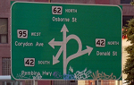 The infamous confusion corner street sign in Winnipeg. The sign shows four arrows crossing one another, each points to a different road.