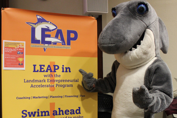 Image of Finn the Shark mascot giving a thumbs up while standing next to a LEAP poster. 