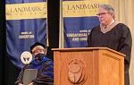 Michael Luciani at podium during Fall 2020 Commencement with Gail Gibson Sheffield seated and watching him. 