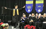 graduating student walking to podium with arms spread wide in celebration