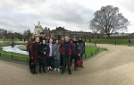 A group shot in Kensington Park. They are standing just in front of a monument surrounded by a small moat. In the far background is Kensington Castle. 