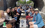 Students on the Netherlands study abroad trip posing for a photo while riding on a boat about to go under an arched foot bridge. 