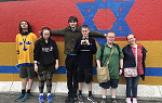 Six students stand in front of a multi-colored mural with a blue Star of David