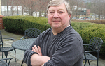 Image of John Wood posting for camera outdoors with his arms folded in front of him. 