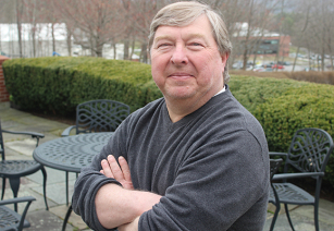 Image of John Wood posting for camera outdoors with his arms folded in front of him. 