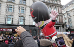 Giant inflatable balloon figure wearing red coat and black hat in parade