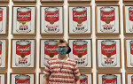 Student standing in front of Andy Warhol soup can painting while wearing a shirt with a print of the same piece of art. 