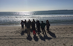 A photo of students on the Summer 2018 Study Abroad trip to New Zealand standing on the beach with the sun setting over the ocean's horizon. 