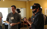 A Virtual Reality demo with one person on the left looking at something off camera and a second person wearing the VR goggles. 