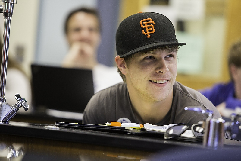 Student in baseball cap smiles while seated at science lab table