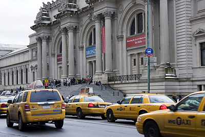 A view of the Metropolitan Museum of Art with yellow taxis lined up in front of it.
