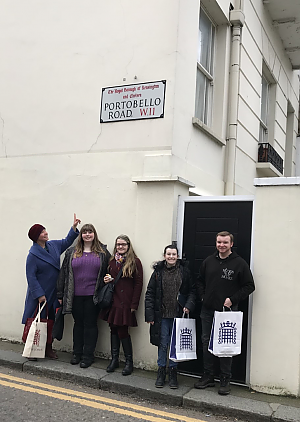 Students lean against a white wall on the streets of London. One of them is pointing up at a sign that reads Portobello Road.