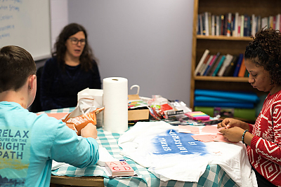 Students sitting around a table making t-shirts with empowering slogans for Sexual Harassment Awareness Day 2017. 