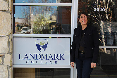 Sandra Fishler, a woman with short dark hair and glasses, stands next to sign for the Landmark College Success Center, placed in a window at the building's entrance.