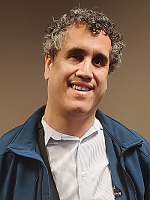 Headshot of man with slightly curly gray-black hair smiling