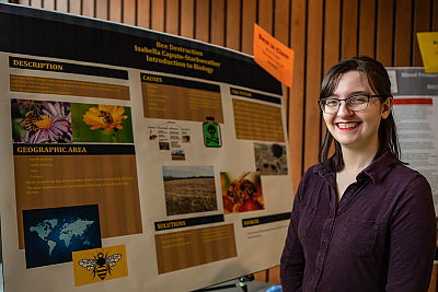 Female Student smiling and standing in front of informational poster that has 