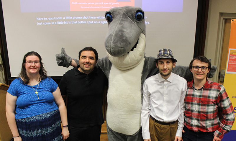 Four students posing for camera with Finn the Shark mascot