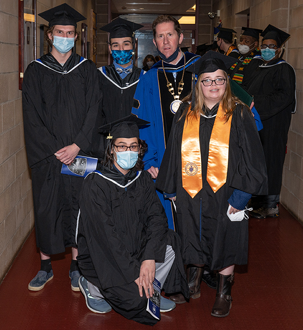President Peter Eden posing with group of students in graduation caps and gowns before December 2021 Commencement ceremony